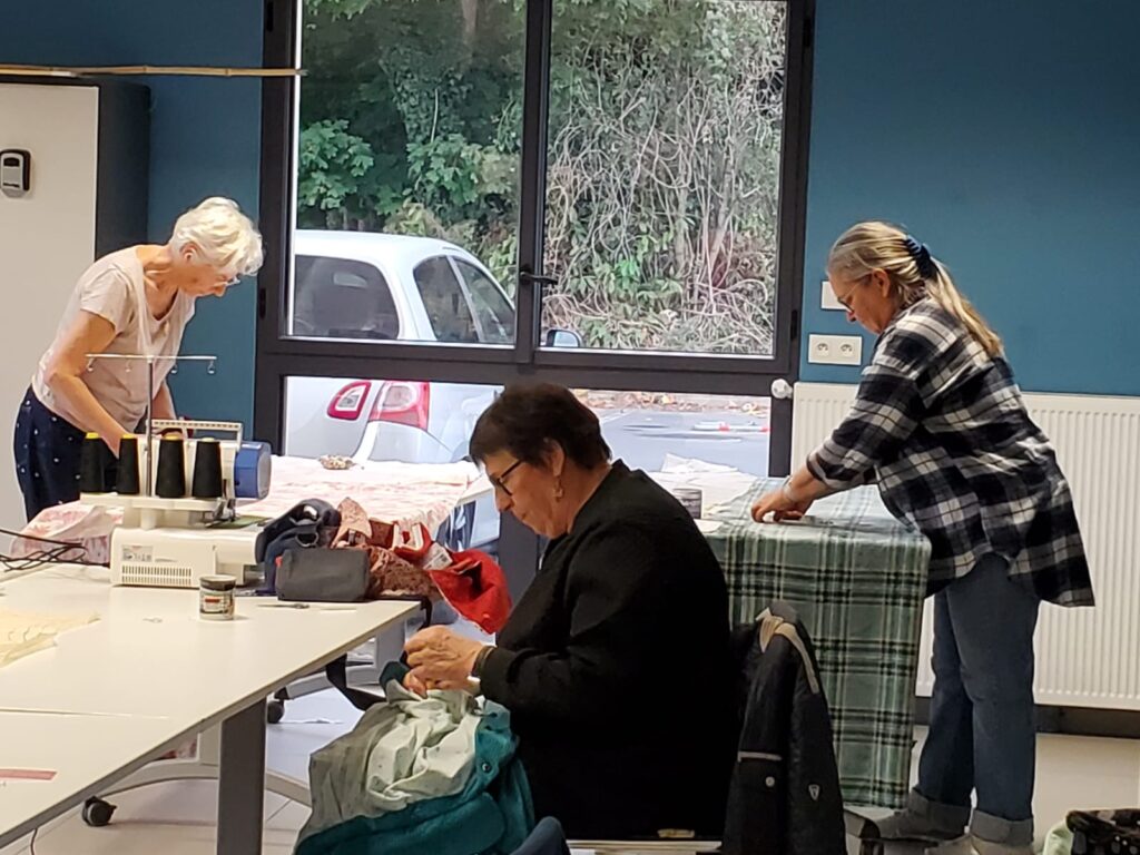 Participantes à la surjeteuse et à la table de coupe devant la baie vitrée
